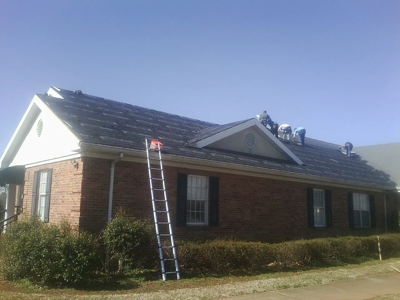Crew tearing shingles off a brick ranch roof with a ladder set — Emergency Roof Repair work by our crew in Avon Lake