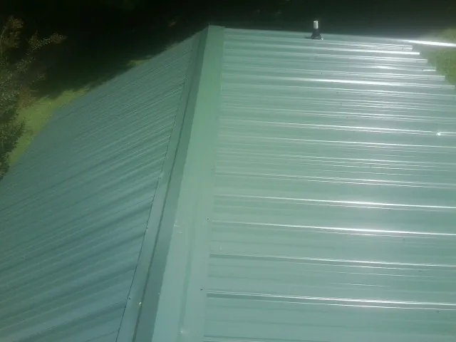 New green metal panels meeting at the ridge of a roof — Flat Roof Repair work by our crew in Avon Lake