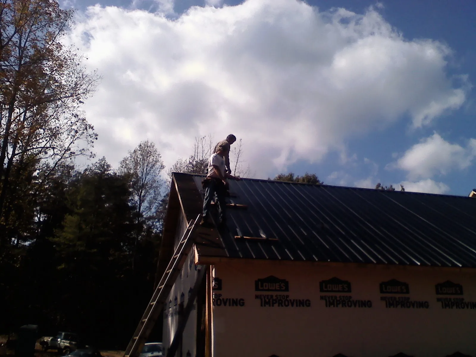 Roofer fastening dark metal panels high against a cloudy sky, from a Roof Inspection job in Avon Lake