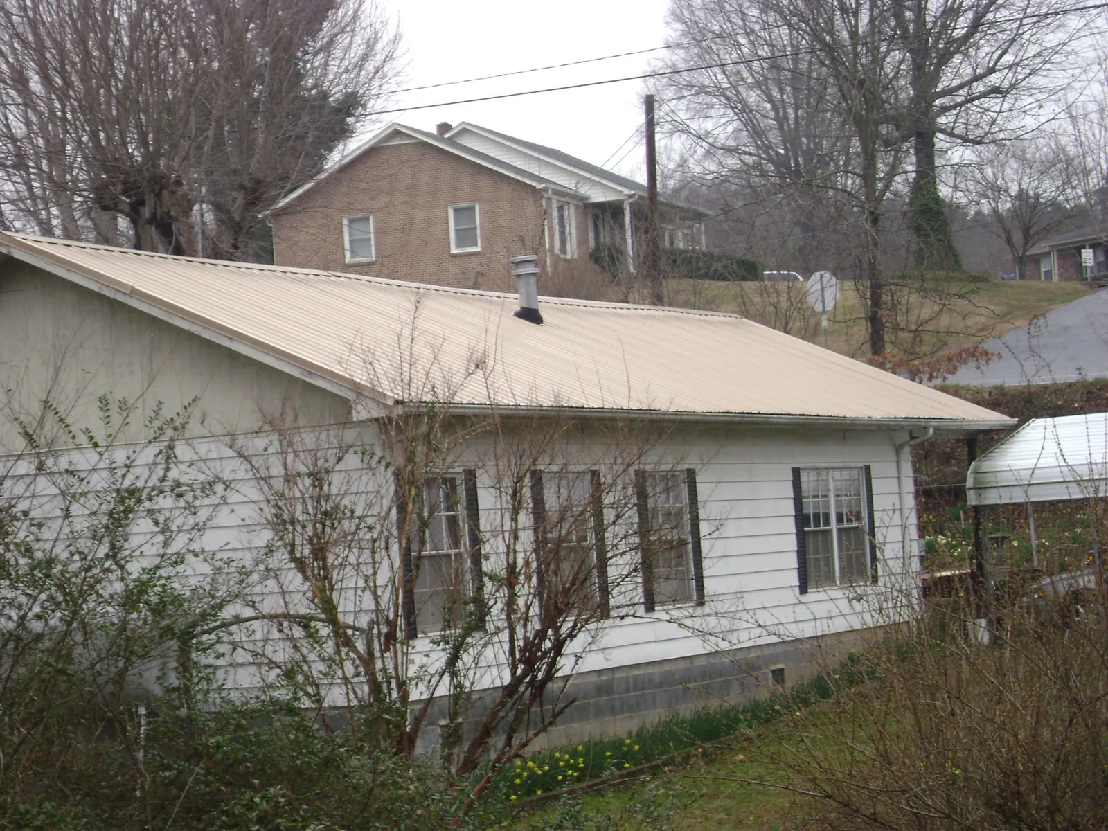Tan metal roof on a white sided house set into a hillside — Commercial Roofing by Roofing Brothers in Avon Lake